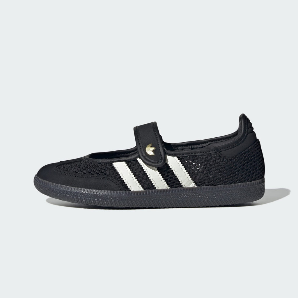 A black knit slip-on adidas samba jane shoe with three white stripes and a hook-and-loop strap featuring a gold adidas logo, shown from the side on a light gray background.