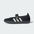 A black knit slip-on adidas samba jane shoe with three white stripes and a hook-and-loop strap featuring a gold adidas logo, shown from the side on a light gray background.