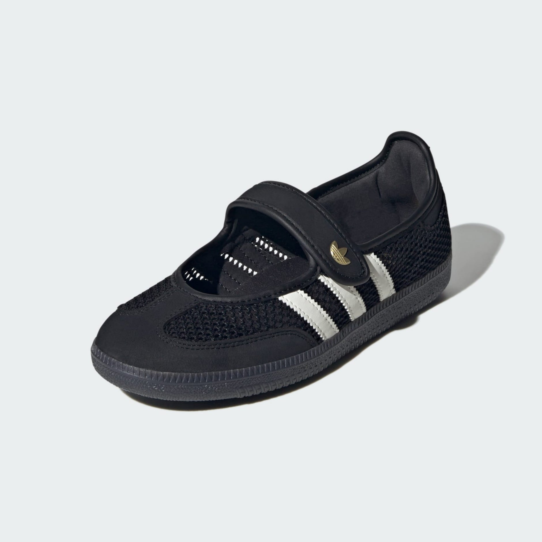 A black Adidas Samba jane shoe, featuring a mesh upper, hook-and-loop strap closure, and the signature three stripes on the side, set against a light gray background.