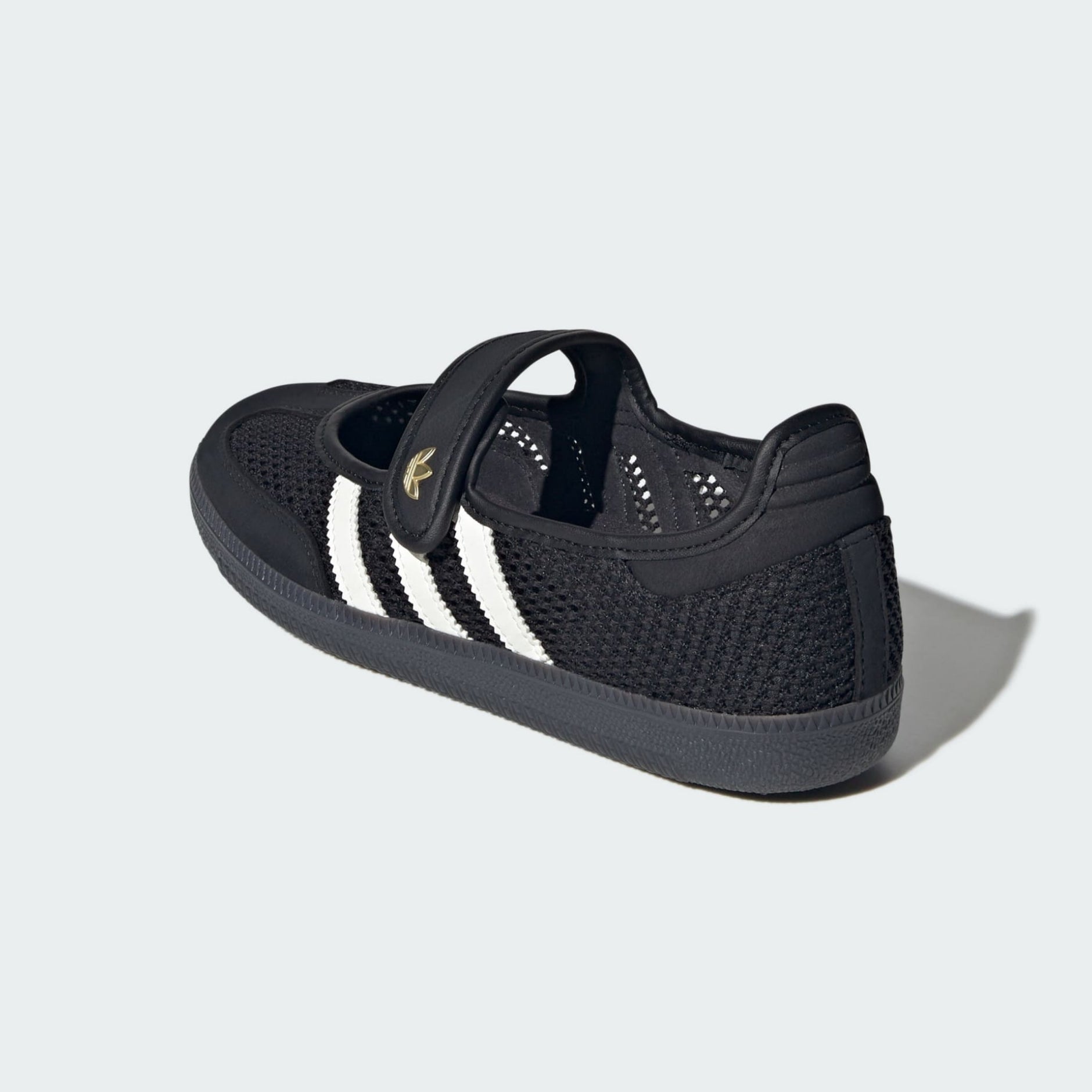 A black mesh low-top sneaker with three white stripes and a gold adidas logo on the side, shown from a three-quarters rear angle on a light gray background.