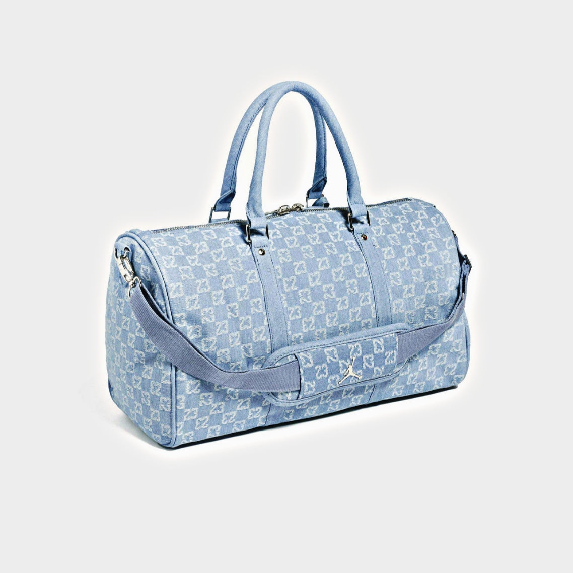 A light blue monogram duffel bag with matching blue handles and shoulder strap, featuring a repeating monogram pattern and silver-tone hardware, photographed on a light gray background.