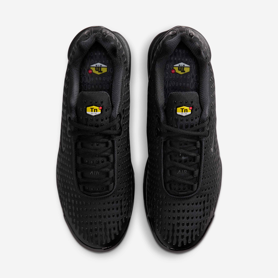 A pair of black athletic sneakers shown from a top-down view against a light gray background. The shoes feature a textured, perforated upper, black laces, and a small yellow and black 'TN' logo on the tongue.