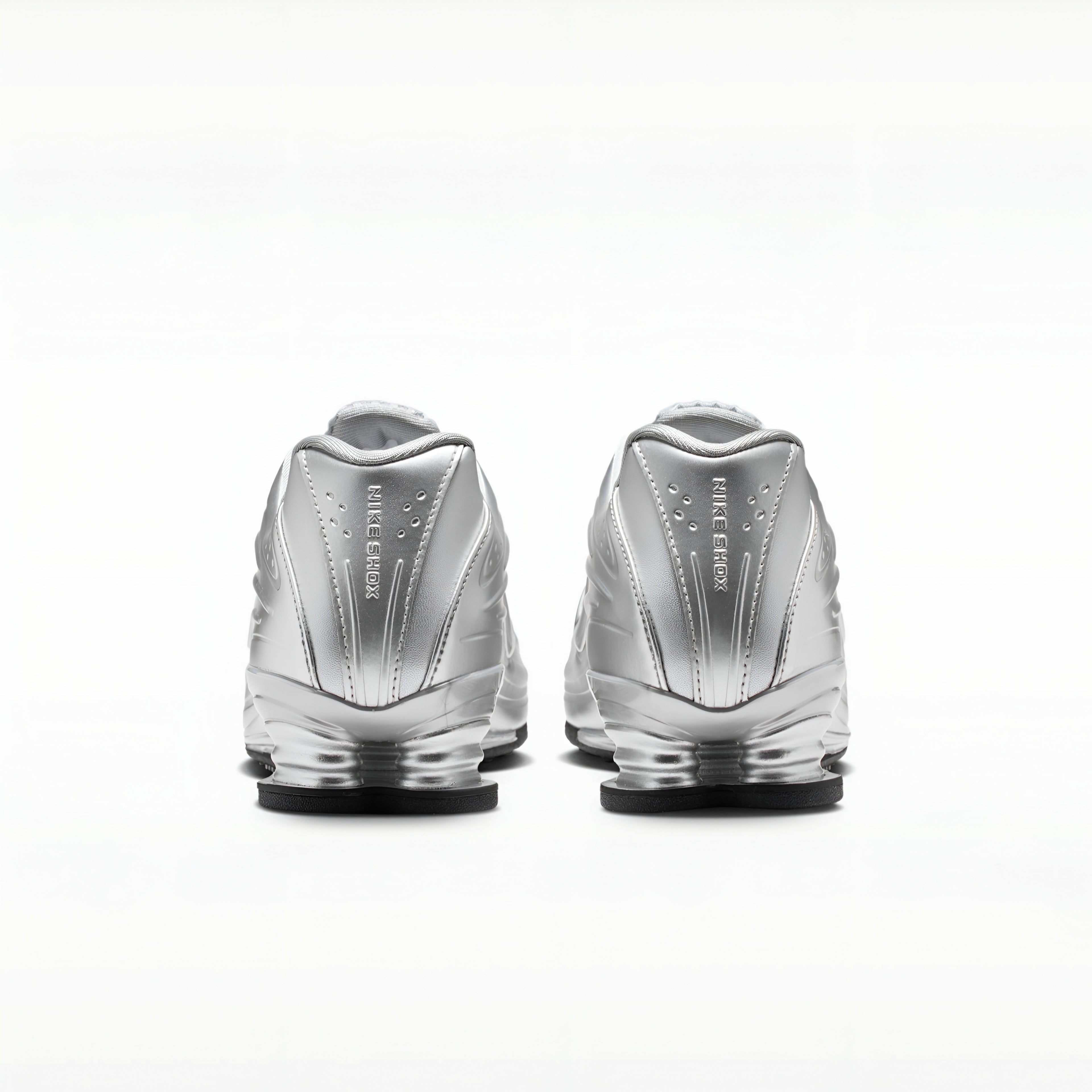 A pair of metallic silver Nike RMX sneakers shown from the back, featuring the 'FIRST STEP' branding and a clear cushioned sole, set against a plain white background.