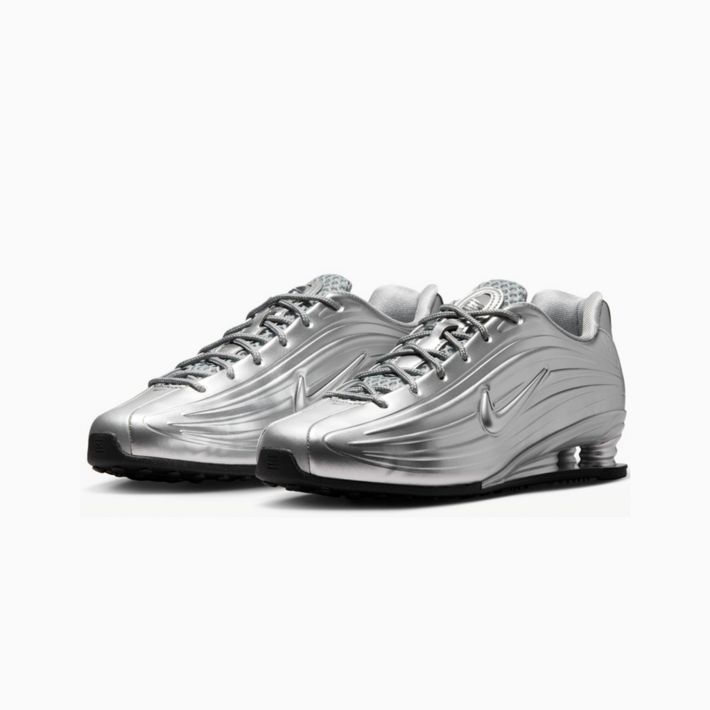 A pair of metallic silver Nike Shox sneakers with black soles, displayed on a clean white background.